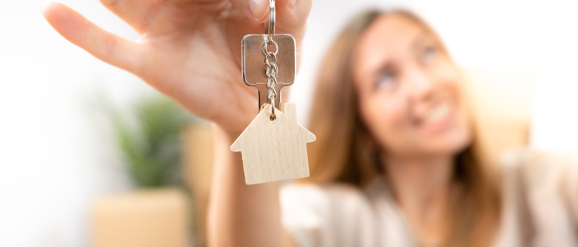 Happy young woman smiling with the new home keys keychain with wooden house real state banner